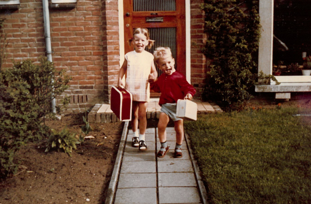 Een foto uit Coralinde's kindertijd waar Coralinde samen met haar broer met koffers lachend rennen op een oprit richting de camera